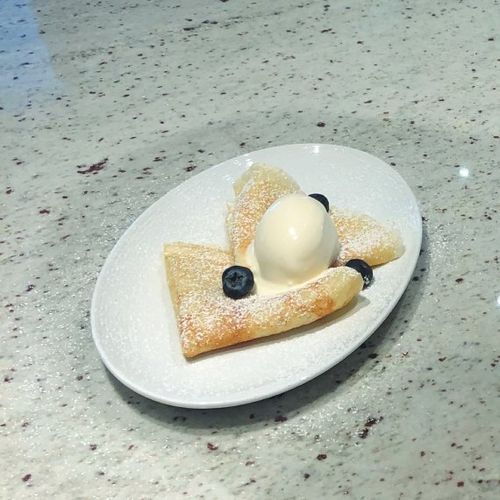 French crepes dusted with powdered sugar and topped with allspice ice cream and blueberries.